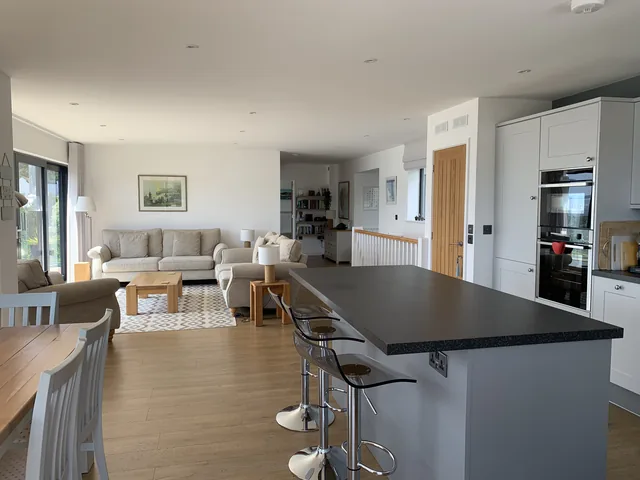Kitchen island and dining table, with sofas beyond and wooden flooring.